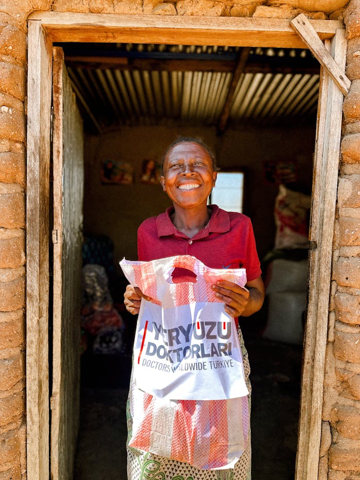 Smiling woman holds donation bag from Doctors Worldwide Turkey in a rustic setting.